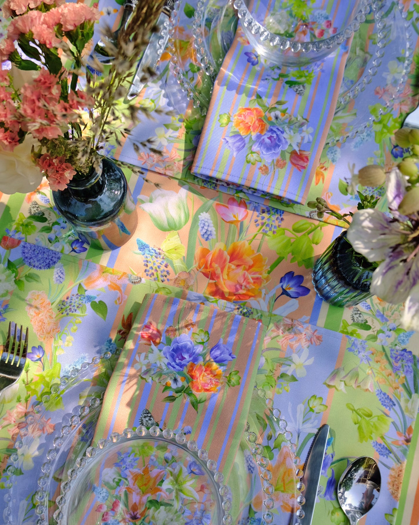 Colourful tablecloth with floral patterns, cutlery, and decorative items on a table.