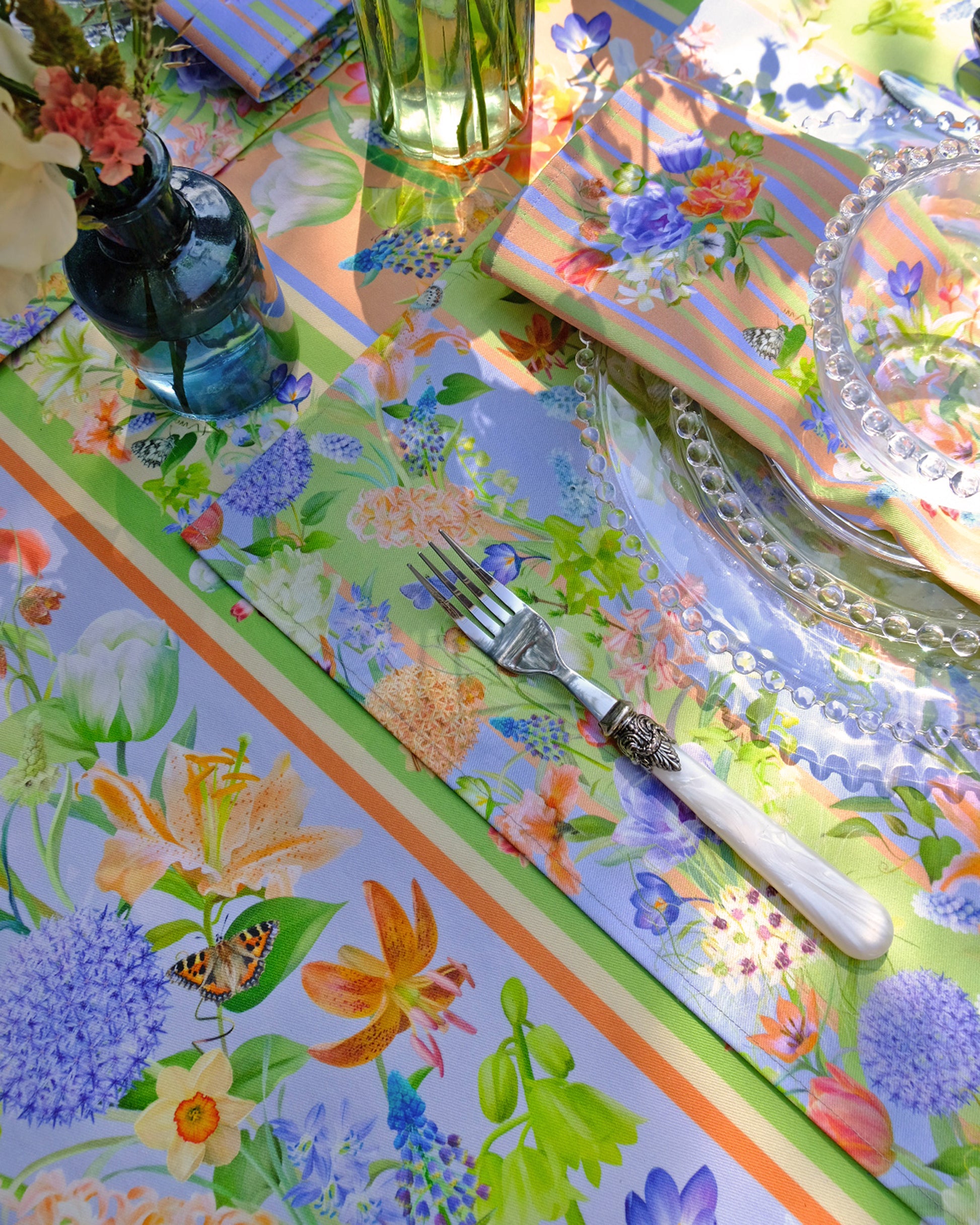 Colourful floral tablecloth with cutlery and glassware on a table.