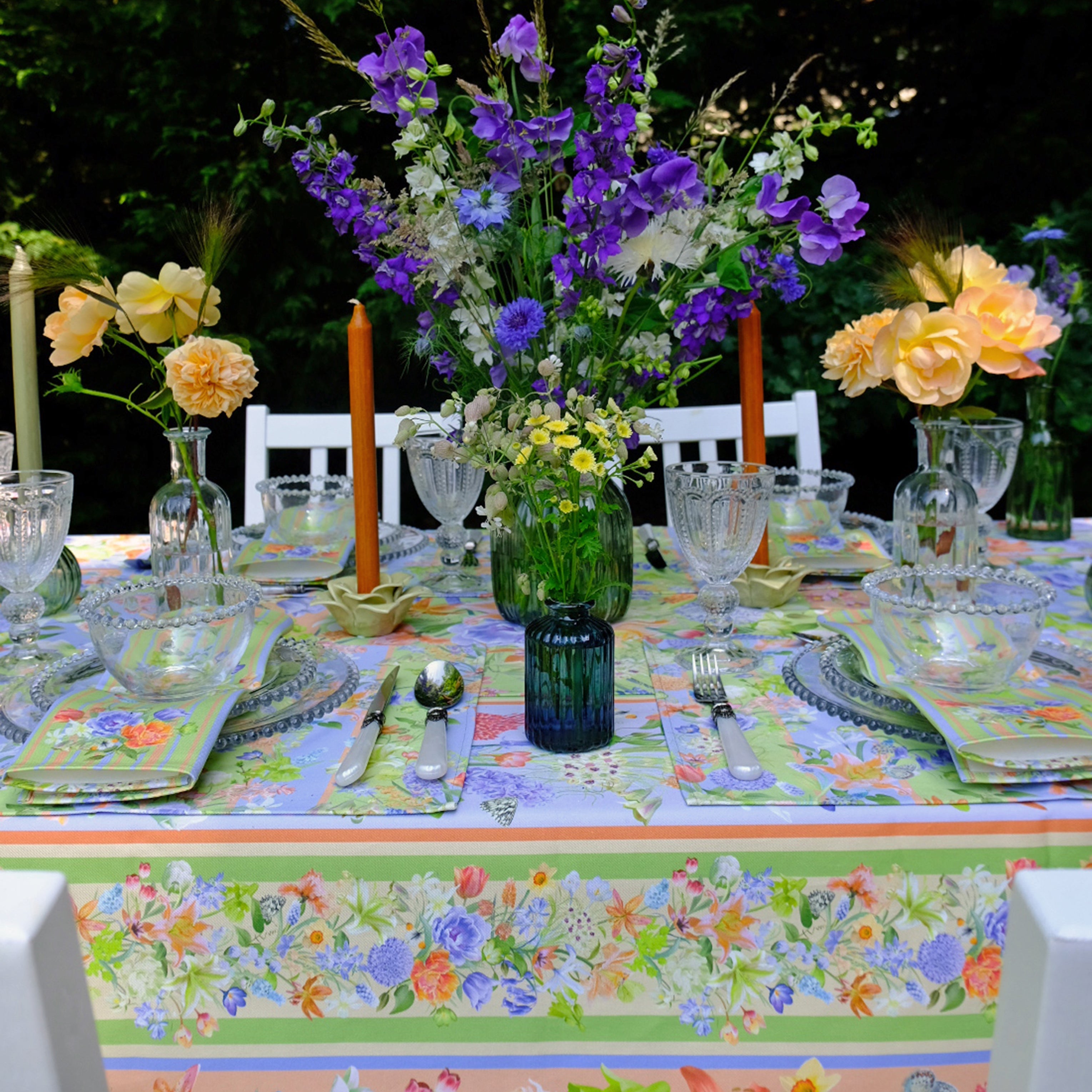 Decorative outdoor table setting with flowers, candles, and colorful tablecloth.