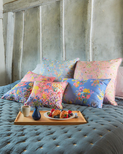 Decorative cushions in Burst Into Bloom statement sea blue botanical fabric arranged on a bed with layered textiles and accessories.