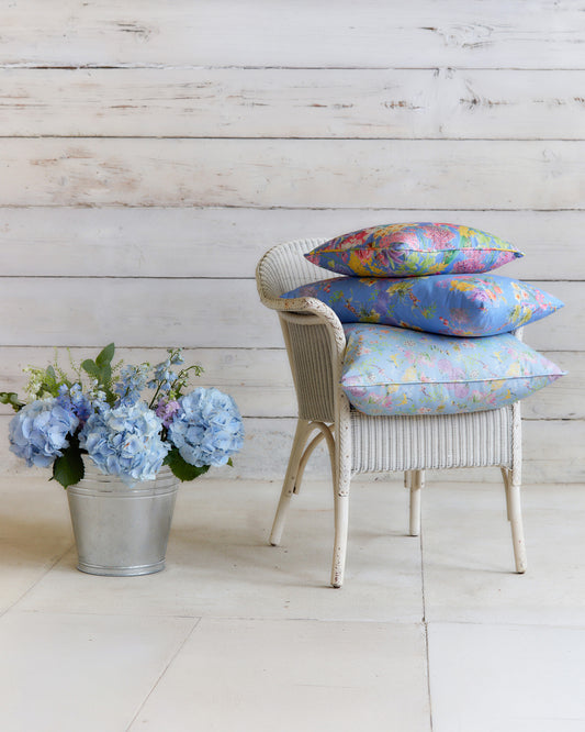 Burst into Bloom Blue floral cushions by Bauldry Botanicals displayed on a white wicker chair, showcasing colourful botanical fabric for home interiors.