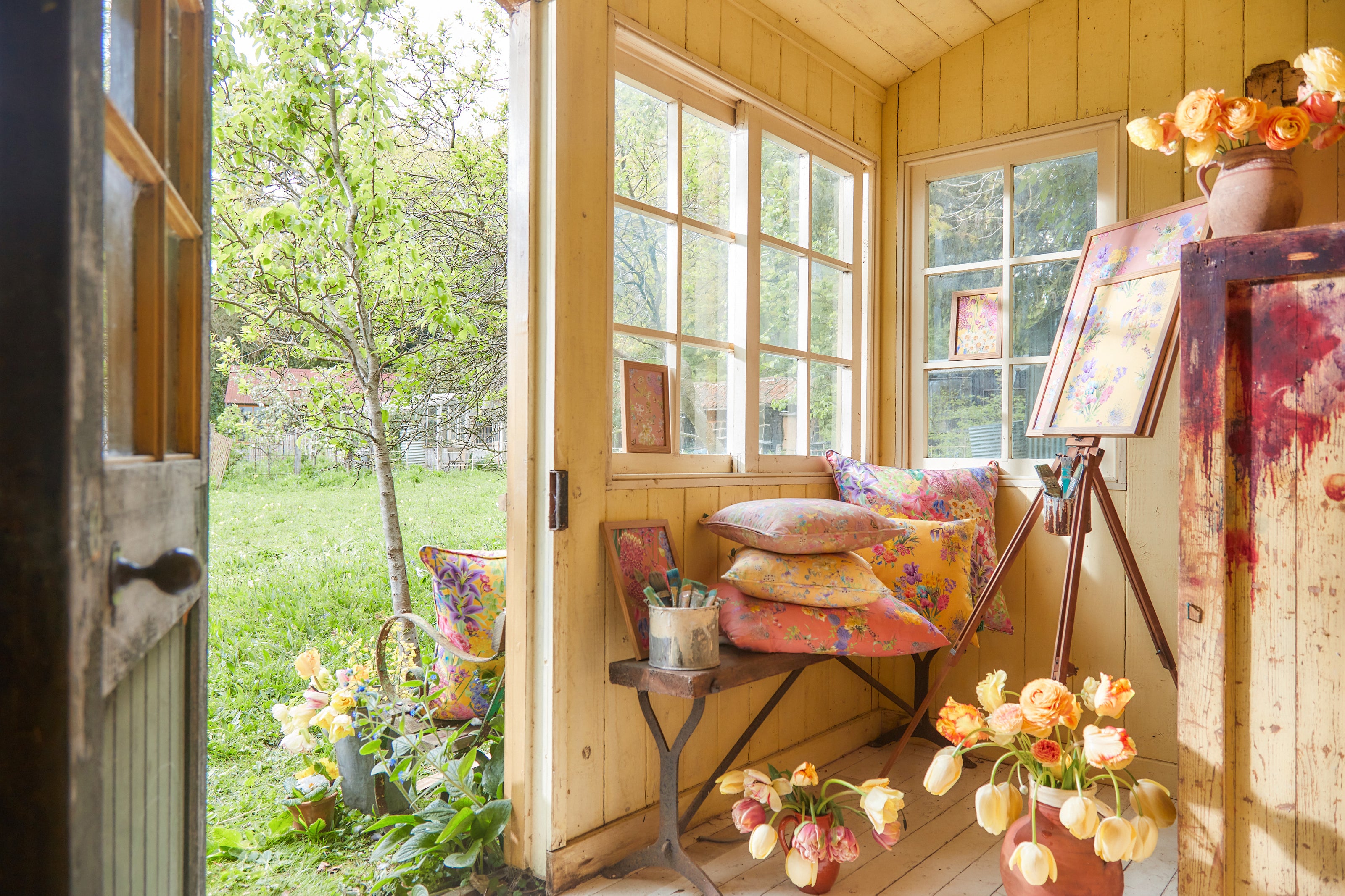 Burst Into Bloom floral fabric displayed in a light filled artists studio surrounded by flowers, painting and creative materials.