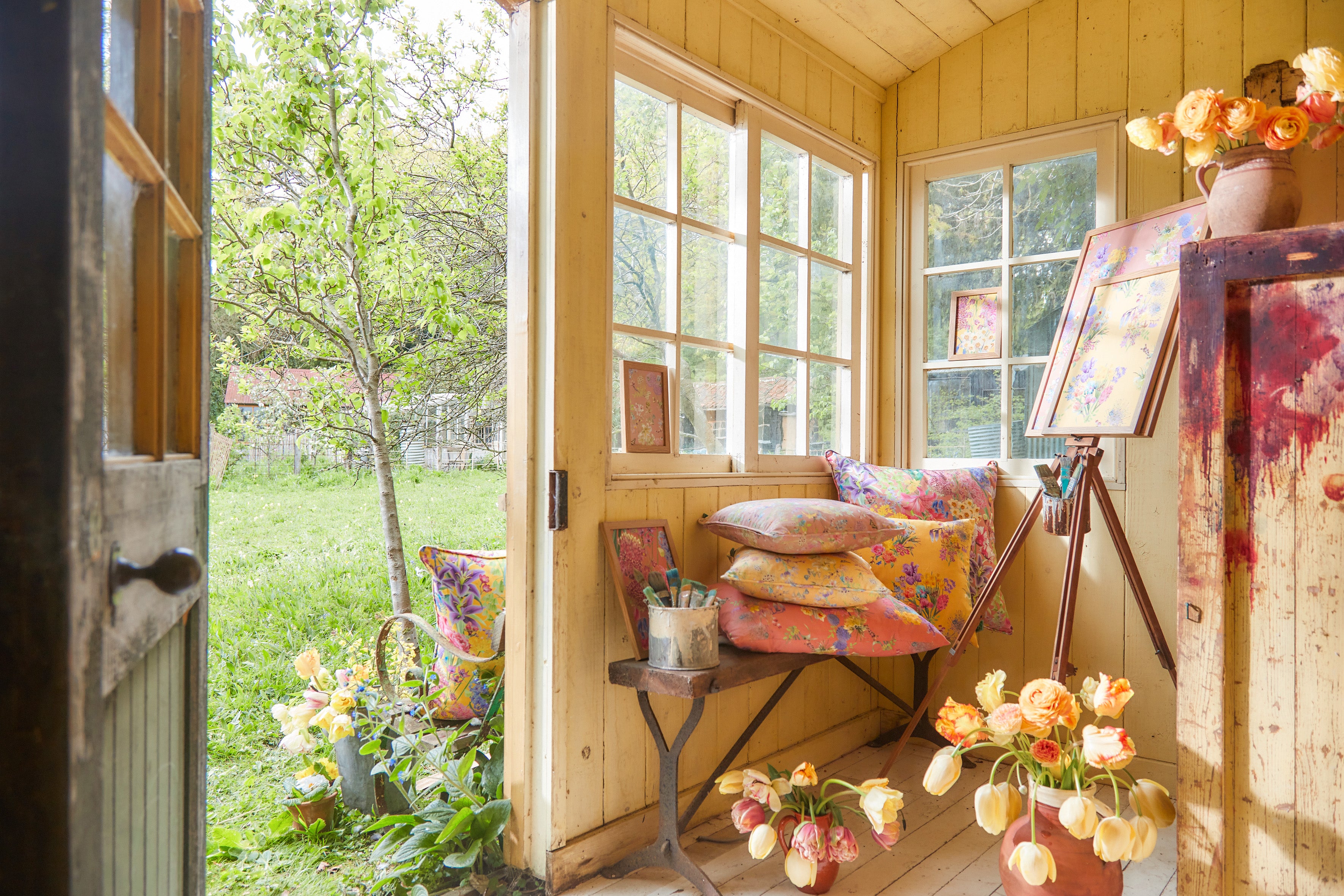 Burst Into Bloom floral fabric displayed in a light filled artists studio surrounded by flowers, painting and creative materials.