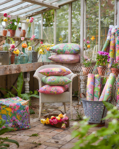Colourful floral cushions and wallpaper in a garden greenhouse setting with Burst Into Bloom Green botanical fabric used for curtains and decorative cushions.