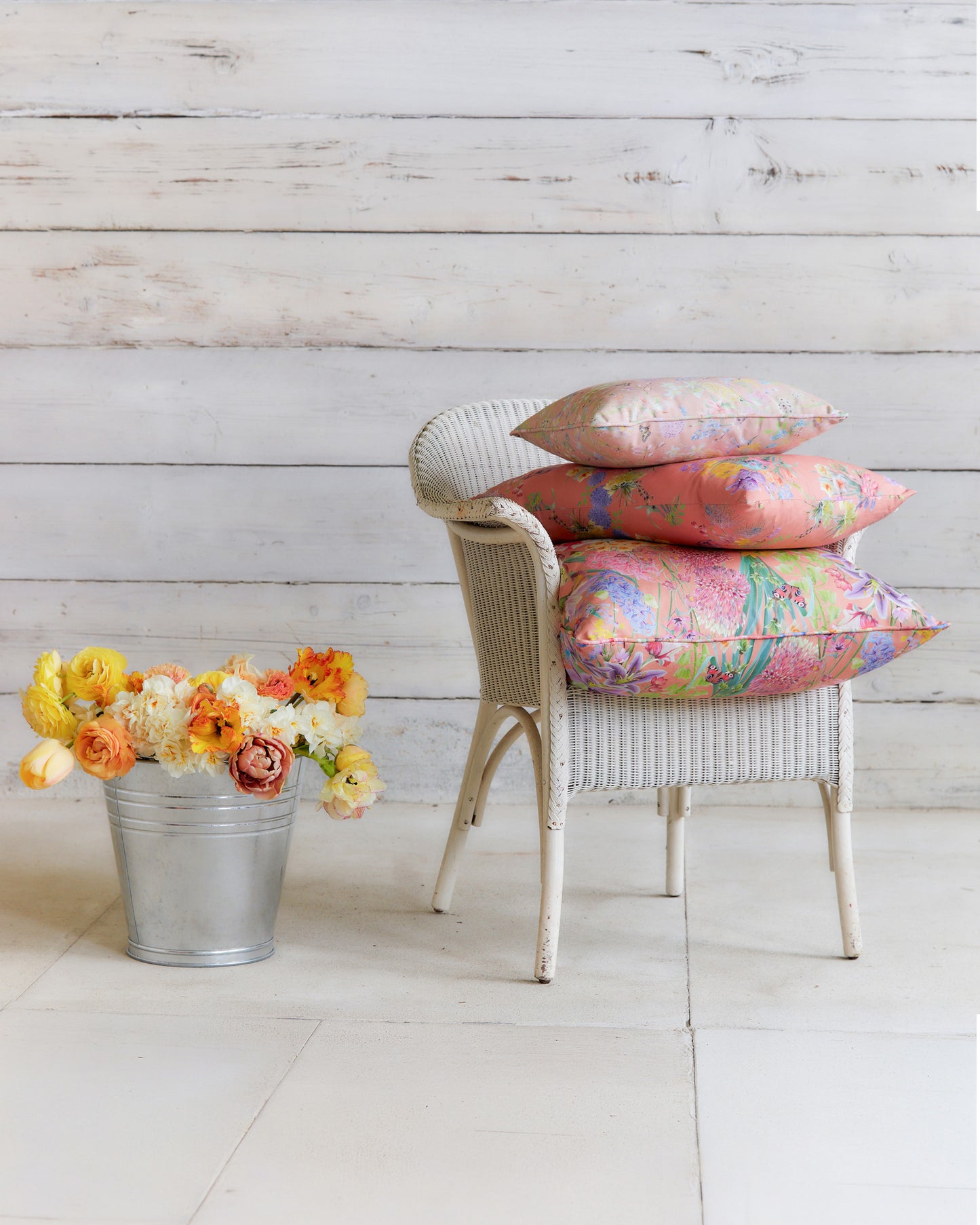 Burst into Bloom Peach floral cushions by Bauldry Botanicals displayed on a white wicker chair, showcasing colourful botanical fabric for home interiors.