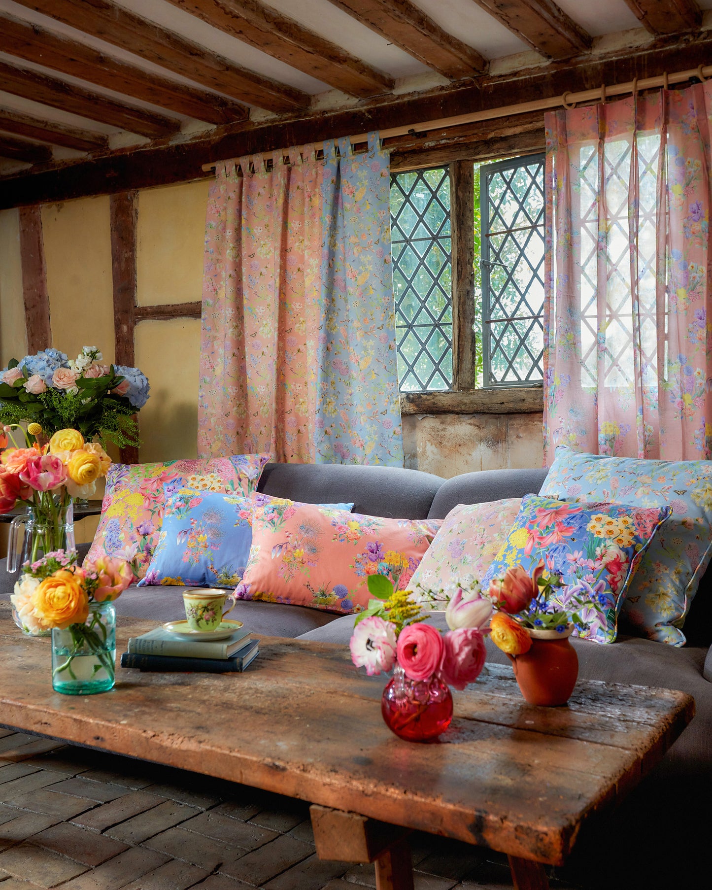 Burst Into Bloom vibrant peach floral fabric used for cushions in a cosy country living room with warm wood interiors.