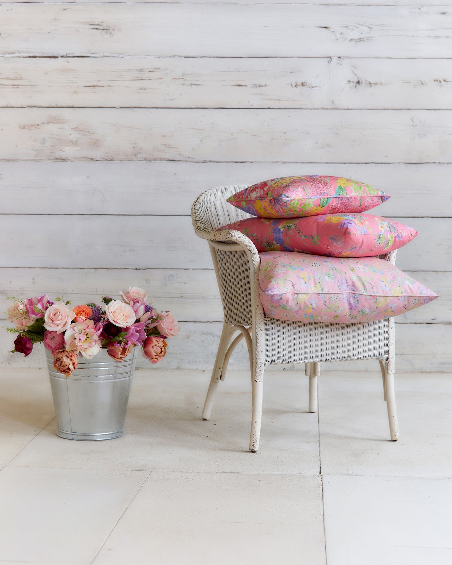 Burst into Bloom Pink floral cushions by Bauldry Botanicals displayed on a white wicker chair, showcasing colourful botanical fabric for home interiors.