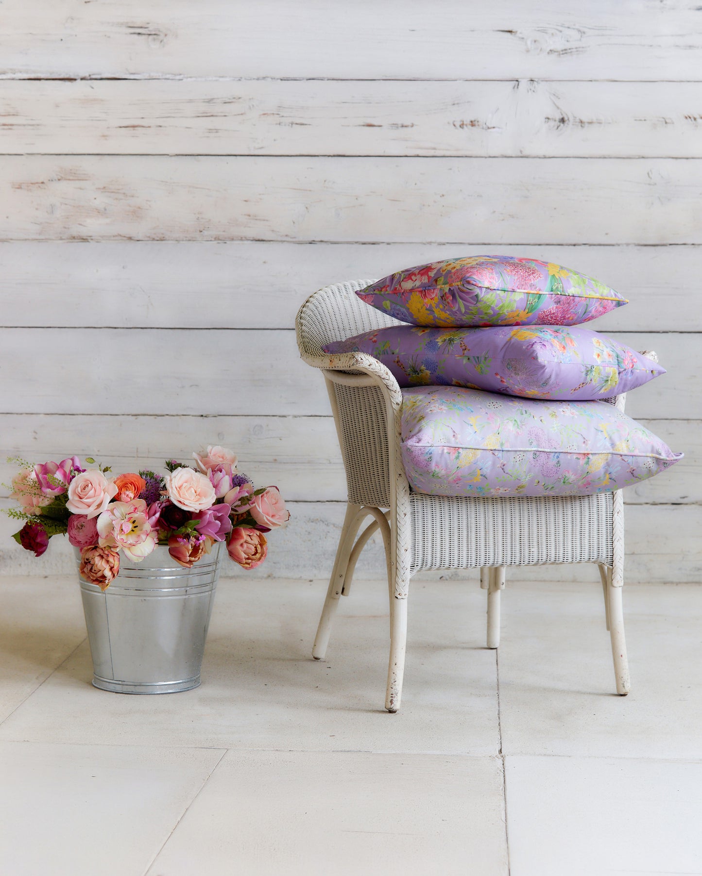 Burst into Bloom Purple floral cushions by Bauldry Botanicals displayed on a white wicker chair, showcasing colourful botanical fabric for home interiors.