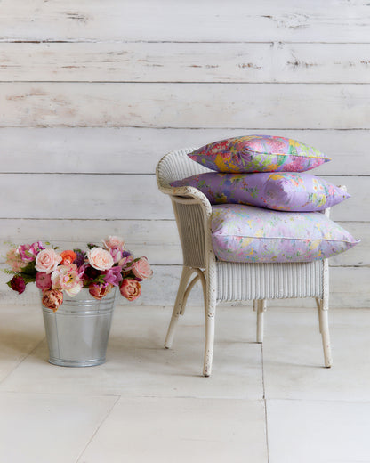 Burst into Bloom Purple floral cushions by Bauldry Botanicals displayed on a white wicker chair, showcasing colourful botanical fabric for home interiors.