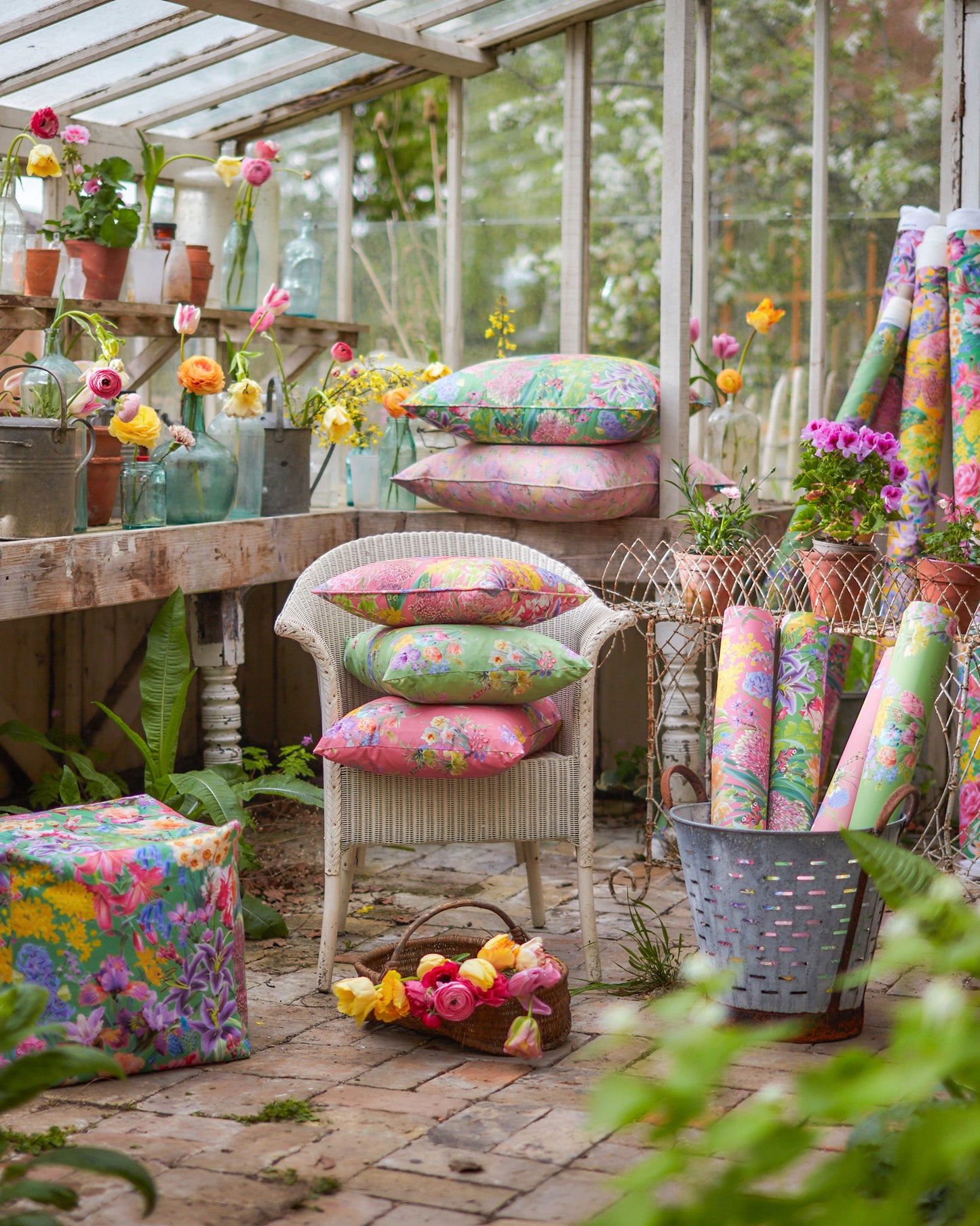 Colourful floral cushions and wallpaper in a garden setting with Hopeful Beginnings pink botanical fabric used for curtains and decorative cushions.