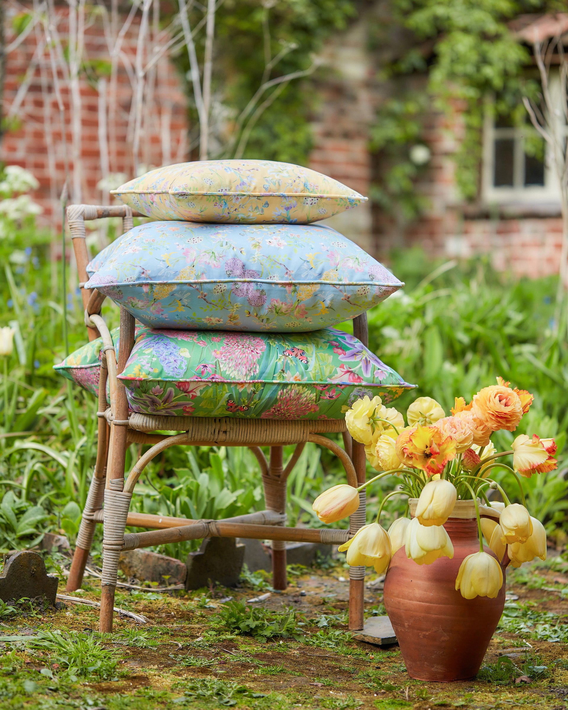 Stack of colourful sustainable floral cushions in Hopeful Beginnings yellow decorated with flowers in a garden setting.