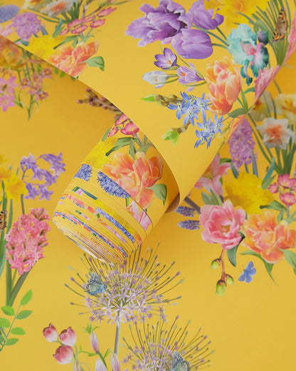A roll of maximalist designer wall covering in gold yellow with a spring botanical print for modern interiors